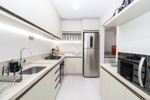 a kitchen with white cabinets and a stainless steel refrigerator at Apartamento Garden Caiobá com Piscina Praia Brava in Matinhos