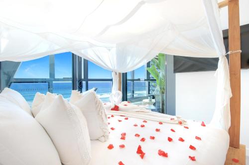 een wit bed met rode rozenblaadjes erop bij Sapphire Oceanview Suite in Gold Coast