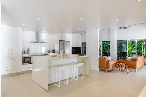 a kitchen with white cabinets and a bar with stools at Serenity Villa with heated POOL & Beach access in Port Douglas
