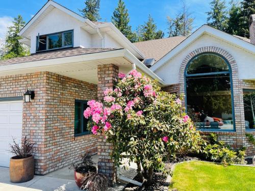 a house with pink flowers in the front yard at The HI-Mark House - Hot tub,AC,Pool table, Pool May2026 in Sicamous