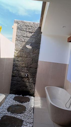 a bathroom with a bath tub and a stone wall at Santika villa ubud in Ubud