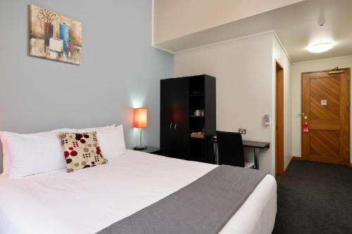 a bedroom with a white bed with a desk and a door at Riverside Hotel Marlborough in Blenheim