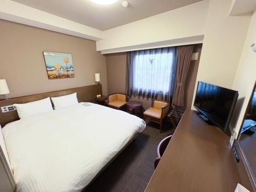 a hotel room with a bed and a flat screen tv at Hotel Route-Inn Tsuruoka Ekimae in Tsuruoka