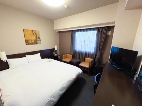 a hotel room with a bed and a flat screen tv at Hotel Route-Inn Tsuruoka Ekimae in Tsuruoka