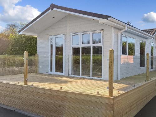 a small white house with a wooden deck at Forrest Lodge in Plumbland