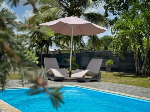 a pair of chairs and an umbrella next to a pool at Villa Jardin secret de la boucan - OFFRE SAISONNIERE ! in Sainte-Rose