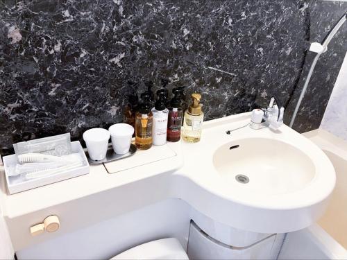 a bathroom with a sink and a toilet with bottles on it at HOTEL LiVEMAX BUDGET Sagamihara in Sagamihara