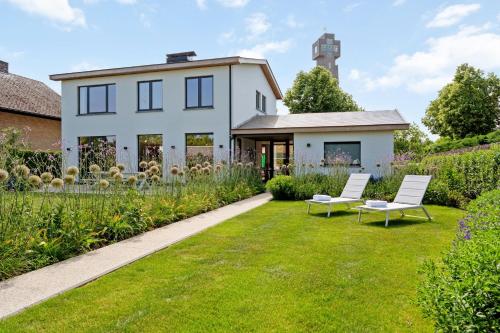 a white house with two white chairs in the yard at Villa Couleur in Diksmuide