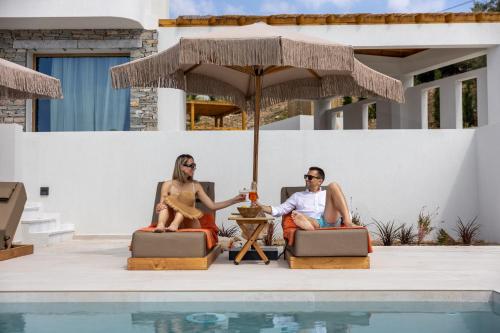 two people sitting under an umbrella next to a pool at La Brise Luxury Suites in Néa Péramos