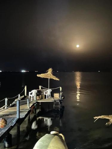 a dock with chairs and an umbrella on the water at night at maison plage kerkennah in Mouamla