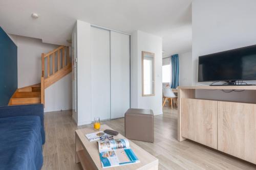 a living room with a blue couch and a tv at Résidence Odalys Le Domaine des Pins in Noirmoutier-en-l'lle