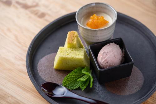 a black plate with a scoop of ice cream and a cup of sauce at 風香る森のホテル鈴桃rindou in Shizuoka