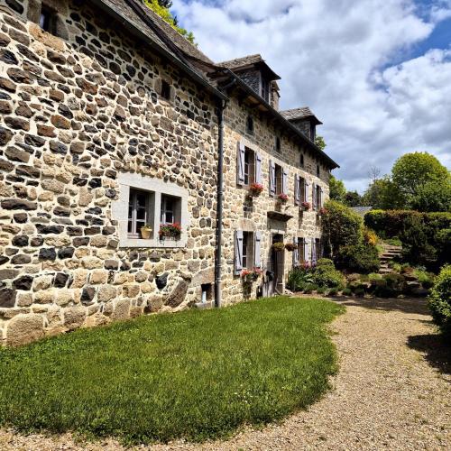 un vieux bâtiment en pierre avec des fleurs aux fenêtres dans l'établissement Le Mas de Rigoulac 5 Chambres d'hotes & SPA sur réservation table d hôtes sauf les mercredis et les dimanches, à Bouyssounouse