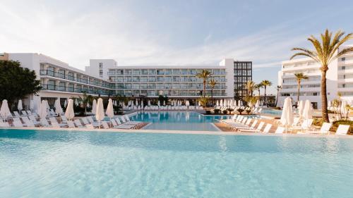 Una gran piscina con tumbonas y un hotel. en AluaSoul Ibiza - Adults only, en Es Canar