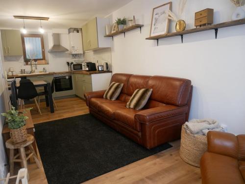 Il comprend un salon avec un canapé en cuir brun et une cuisine. dans l'établissement La Maison Arola, à Bagnères-de-Bigorre