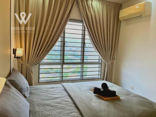 a woman sitting on a bed looking out a window at 5pax Serene 3BR at Simfoni Heights with Batu Caves View in Batu Caves