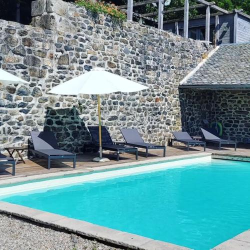 une piscine avec deux chaises et un parasol dans l'établissement Le Mas de Rigoulac Gîte le Four, à Bouyssounouse