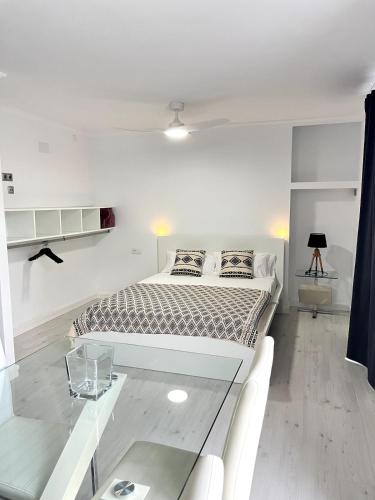 a white bedroom with a bed and a glass table at Apartamento Portus Apostoli in Noya