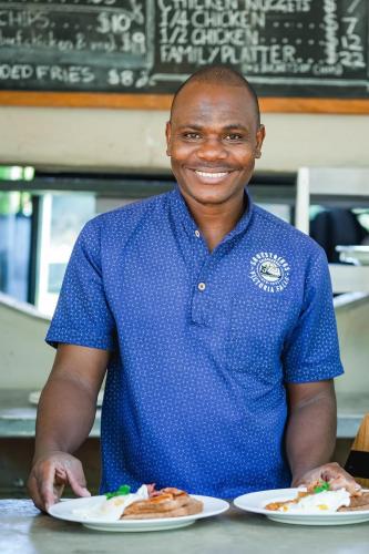a man in a blue shirt holding plates of food at Shoestrings Backpackers Lodge Vic Falls in Victoria Falls