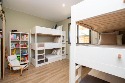 a bedroom with white bunk beds and a chair at La Villa face au Lac in Saramon