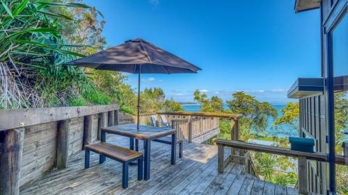 a table and benches on a deck with an umbrella at Rangi Terrace Views in Karikari Peninsula