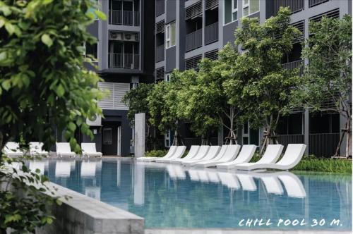 a swimming pool with white chairs in front of a building at Nich Mono Ramkhumheng Low Rise in Sathani Ban Hua Mak