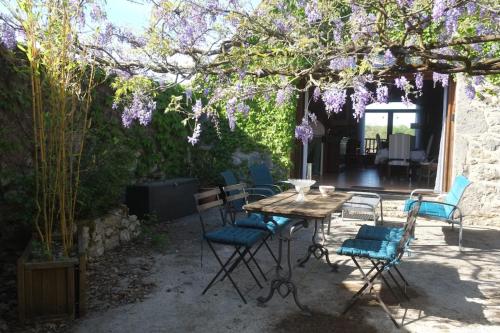 une table et des chaises sous un arbre avec des fleurs violettes dans l'établissement La Sagnarde Loubressac Terrasse intime, à Loubressac