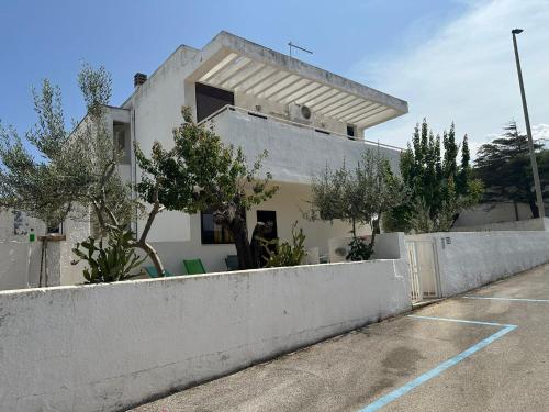 a white building with a fence and trees in a parking lot at Giardino dei Trulli - Villa al Mare in Faccia di Trippa