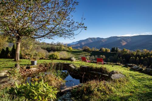 a pond in a field with two red chairs and mountains at Chambres d'hôtes le Clou in Thiézac