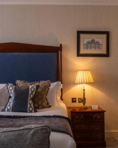 a bedroom with a bed and a nightstand with a lamp at Lucknam Park Hotel in Chippenham