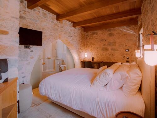 a bedroom with a white bed in a stone wall at Santa Veneranda Suites "by Checkin" in Ayía Paraskeví