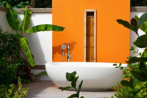 a white bath tub sitting in front of an orange wall at Angsana Velavaru in Dhaalu Atoll