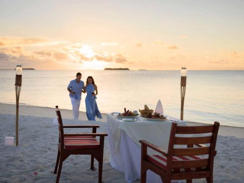 a couple standing on the beach with a table on the beach at Angsana Velavaru in Dhaalu Atoll