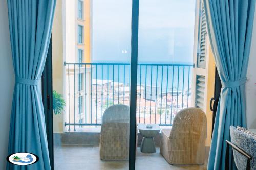a room with a balcony with blue curtains and chairs at Oscar Seaview Apartment in Phu Quoc