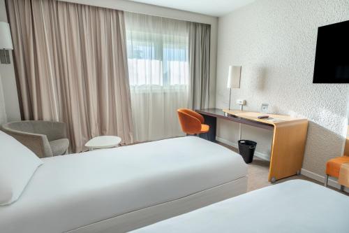 a hotel room with two beds and a desk at Novotel Poissy Orgeval in Orgeval