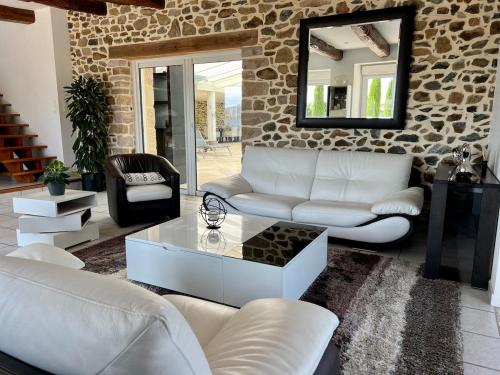 Elle comprend un salon doté d'un mobilier blanc et d'un mur en pierre. dans l'établissement Grande maison en campagne avec piscine, 11 voyageurs, à Hénansal