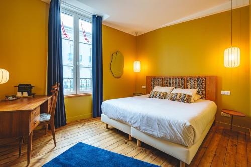 a bedroom with yellow walls and a bed and a desk at The Originals Boutique, Hôtel Le Londres, Saumur in Saumur