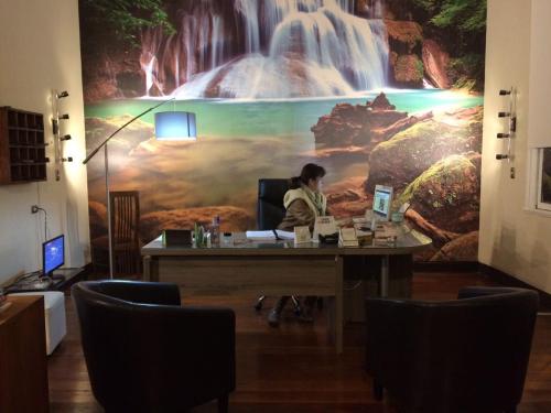 a woman sitting at a desk in front of a waterfall mural at Hotel Casa del Profesor in Iquique