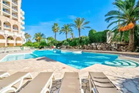 une piscine avec chaises longues et palmiers dans l'établissement Le Cannes Beach 497 - vue mer et piscine Cannes, à Cannes