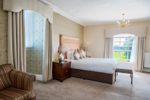 a bedroom with a bed and a chair and a window at Orton Hall Hotel & Spa in Peterborough
