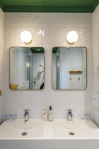 a bathroom with two sinks and two mirrors at The Originals Boutique, Hôtel Le Londres, Saumur in Saumur