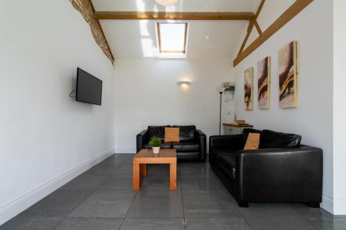 a living room with two black leather couches and a table at Owls Hoot at Tove Valley Cottages in Towcester
