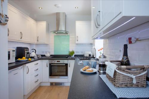 a kitchen with white cabinets and a black counter top at Lapwing 2, The Cove, Waterfront Apartment in Brixham