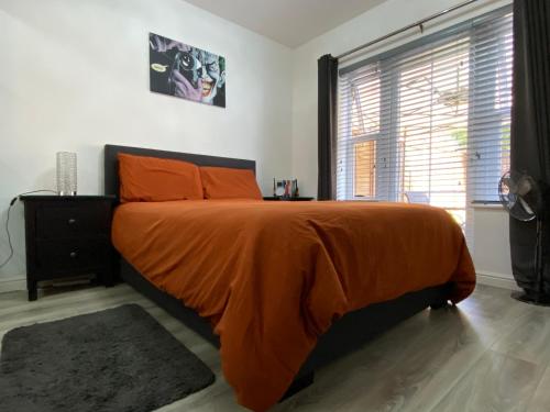 a bedroom with a bed with an orange blanket and a window at Modern 1 bedroom flat with patio garden & parking in Ashford