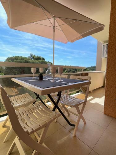 - une table avec deux chaises et un parasol sur le balcon dans l'établissement bel appartement climatisé près de la plage, à Bormes-les-Mimosas