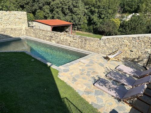 - une piscine avec 2 chaises longues à côté d'un mur en pierre dans l'établissement Maison de village avec piscine, à Saint-Étienne-de-Lolm