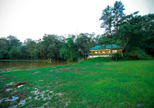 a house in the middle of a field next to a river at Tusker Inn Forest Lodge in Pulpally