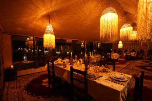a dining room with white tables and chandeliers at Arabian Nights Desert Camp Merzouga in Lac Yasmins