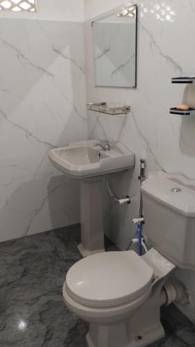 a white bathroom with a toilet and a sink at Oshi villa in Hikkaduwa