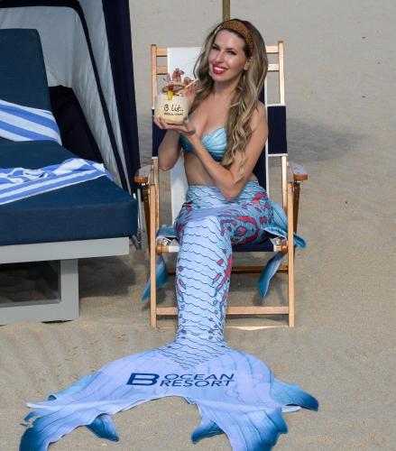 a woman sitting in a chair on the beach holding a cake at B Ocean Resort Fort Lauderdale Beach in Fort Lauderdale